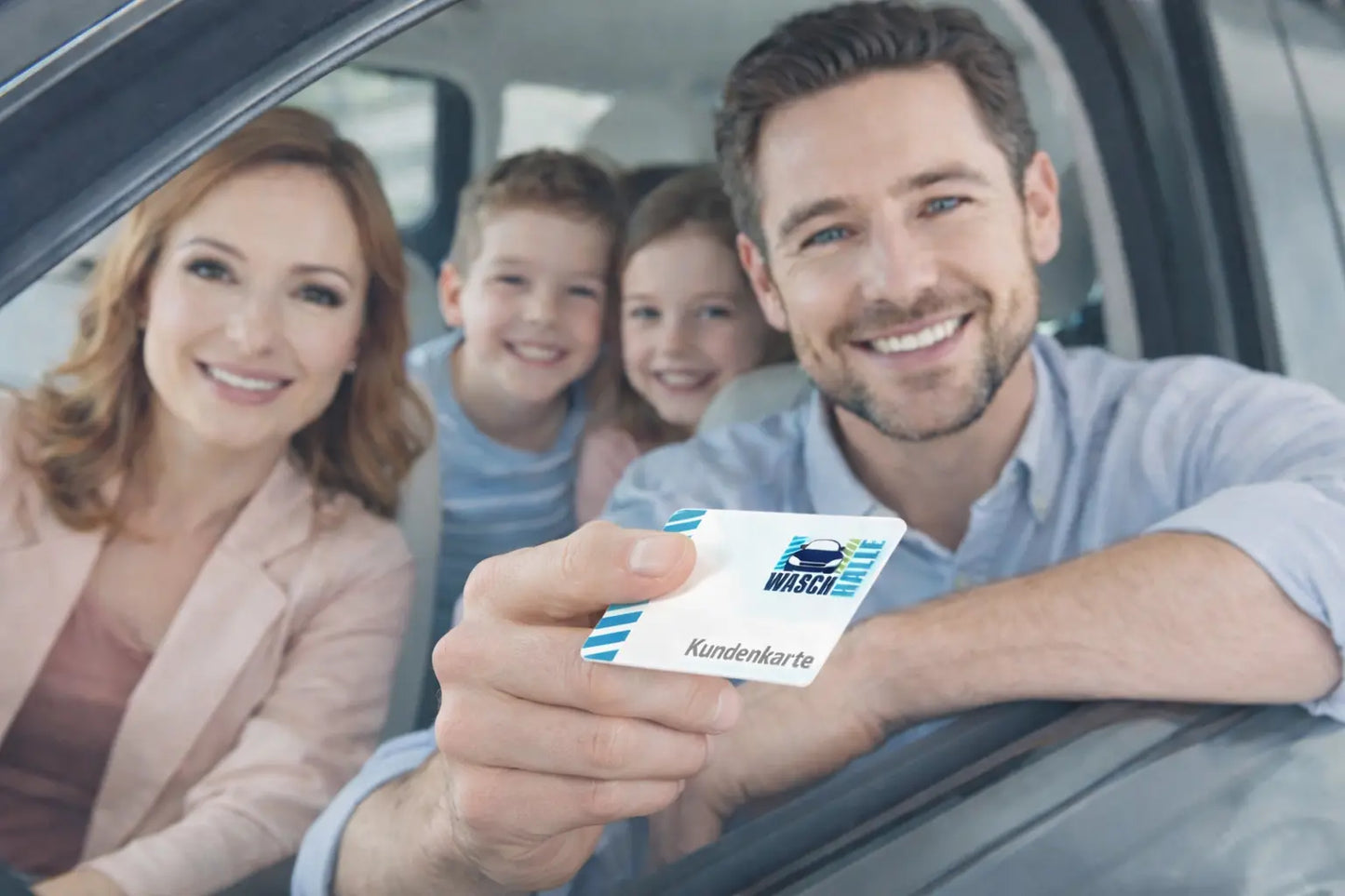 Eine lächelnde Familie sitzt in einem Auto, die Mutter hält die "Waschhalle"-Kundenkarte aus dem Fenster