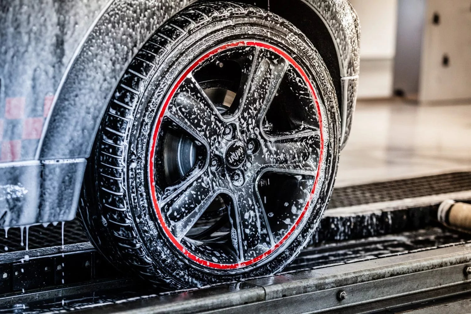 Nahaufnahme eines mit Seife und Schaum bedeckten Autorads mit einem roten Streifen, der die Felge umrandet, während es in einer Innenwaschanlage gewaschen wird.