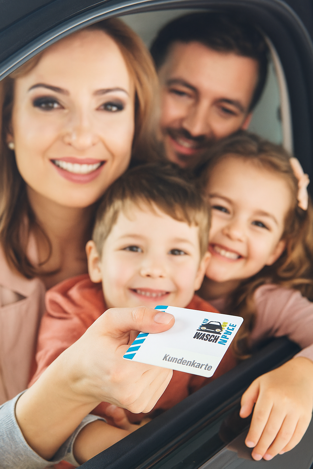 Eine lächelnde Familie sitzt in einem Auto, die Mutter hält die "Waschhalle"-Kundenkarte aus dem Fenster
