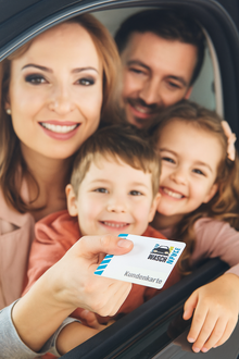 Eine lächelnde Familie sitzt in einem Auto, die Mutter hält die "Waschhalle"-Kundenkarte aus dem Fenster