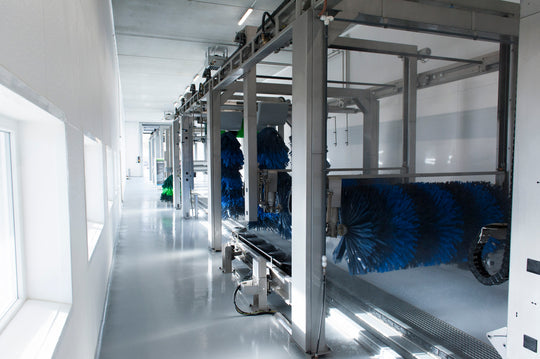 Eine moderne, leere automatische Autowaschanlage mit großen rotierenden blauen und grünen Bürsten, Metallrahmen und heller Beleuchtung, die sich auf dem sauberen, glänzenden Boden spiegelt.