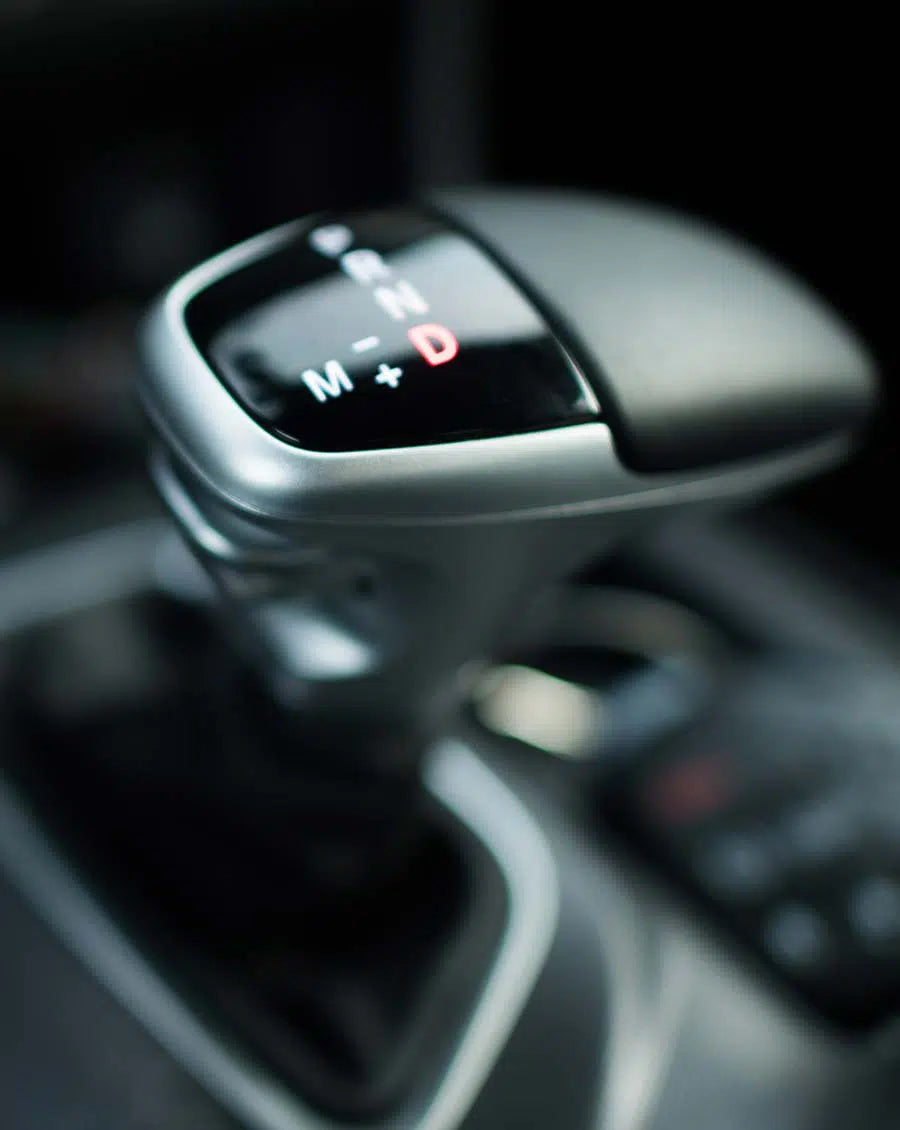 Nahaufnahme des Schalthebels eines Automatikwagens, auf dem die Buchstaben M, +, -, N und D für die verschiedenen Fahrmodi zu sehen sind, wobei der Hintergrund leicht verschwommen ist.